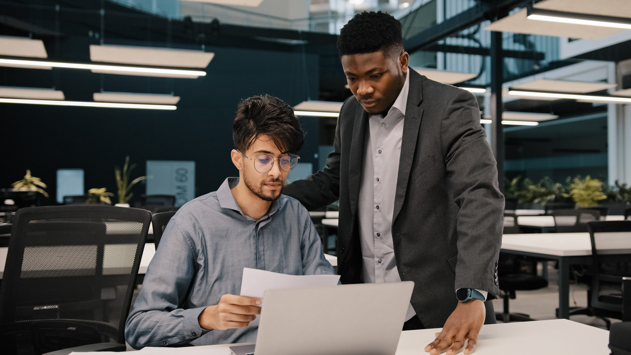 Male african mentor financial advisor businessman boss helping arab man colleague discussing marketing result in report paperwork american supervisor training partner giving business advice at office