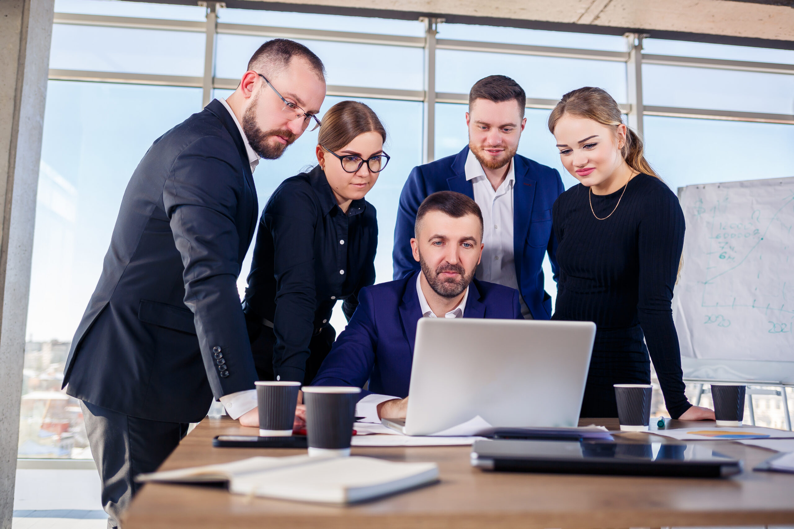 Happy business people looking at laptop presentation, success at work, sitting in modern office